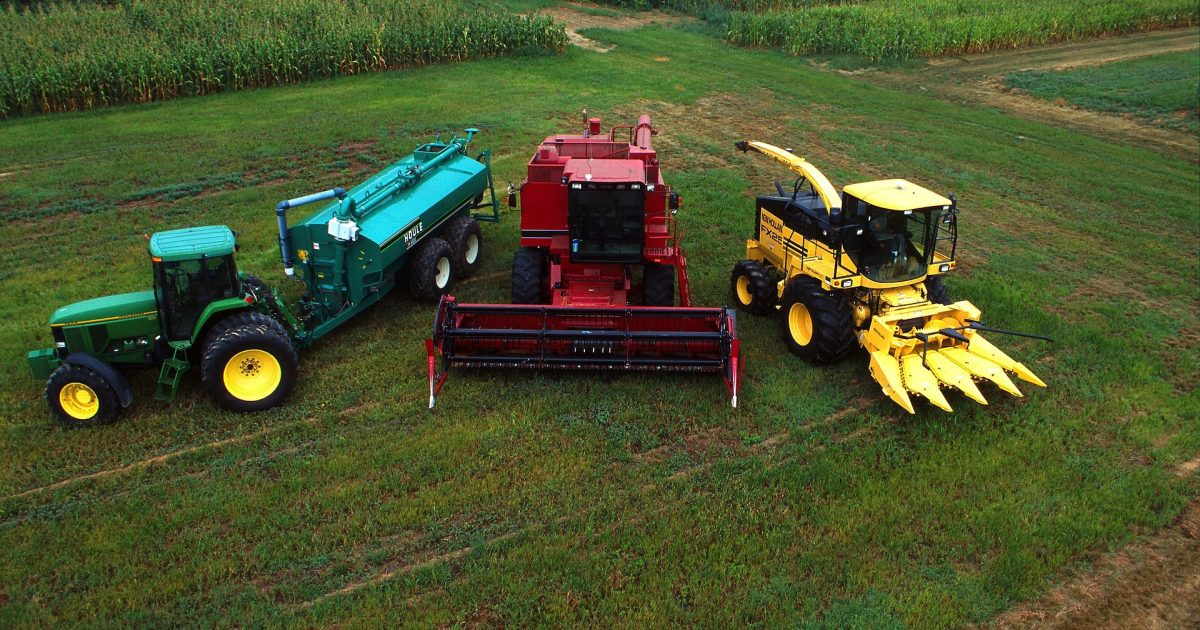 Aerial view of farming equipment including green tractor, red combine harvester, and yellow corn harvester in agricultural field